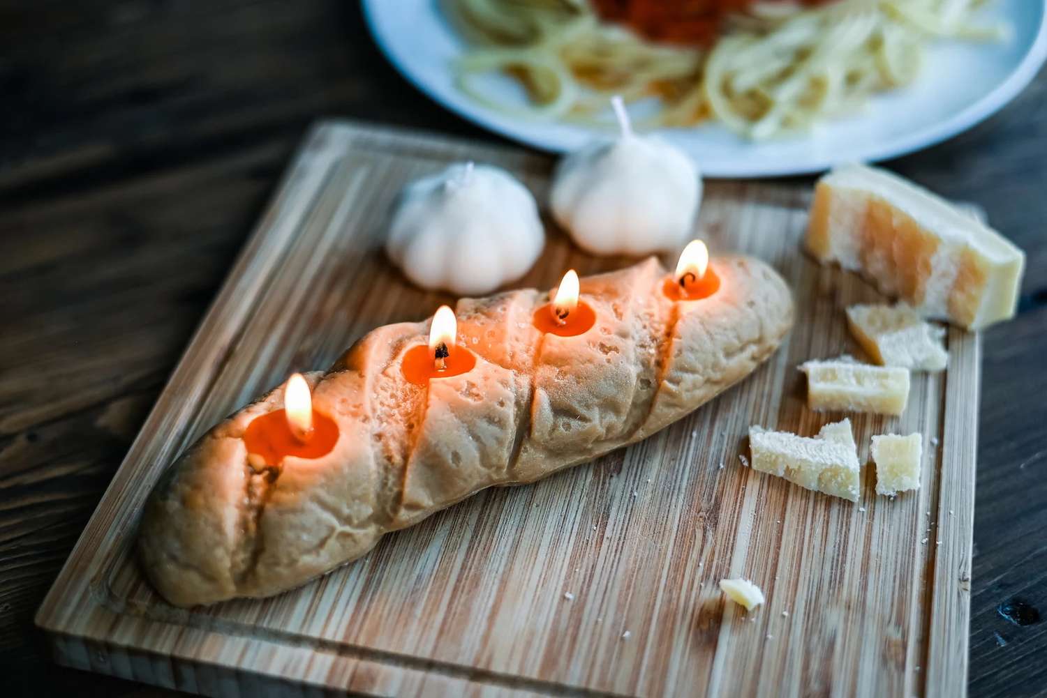 A loaf of bread with candles inserted displayed on a wooden cutting board alongside garlic and pieces of cheese