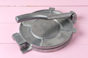 Metallic manual machine tortilla press on wooden pink background