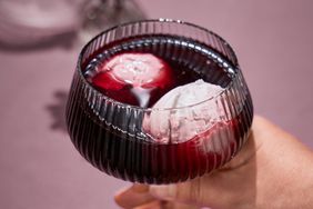 A glass containing red wine and scoops of ice cream being held by a hand