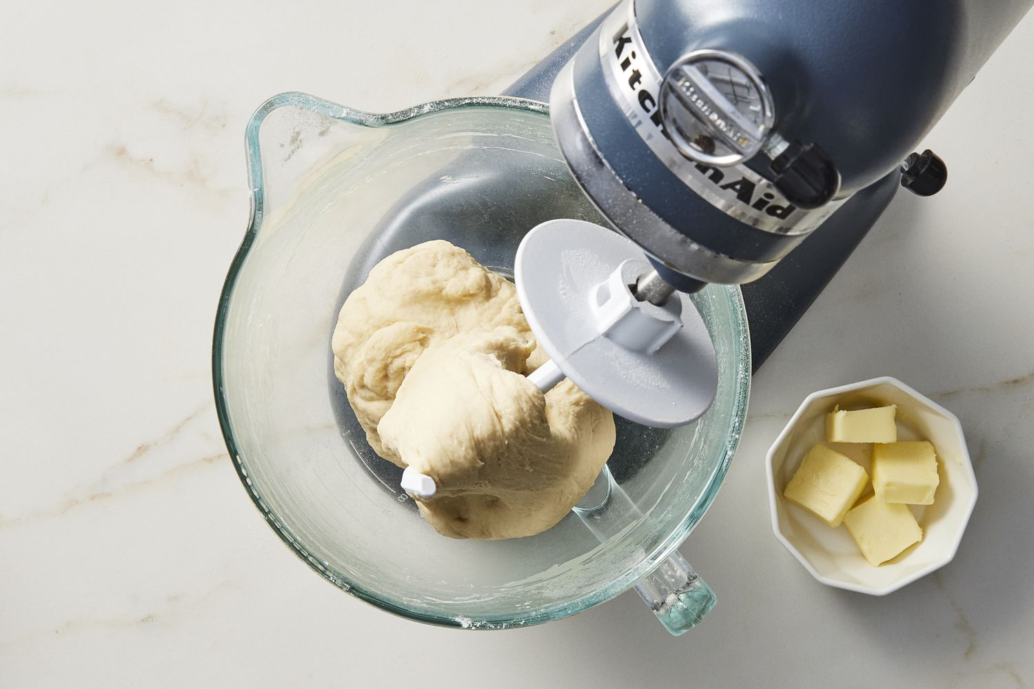 Dough in glass bowl under stand mixer with butter