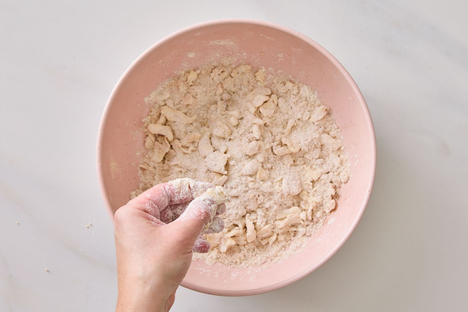 A hand mixing crumbly dough in a bowl