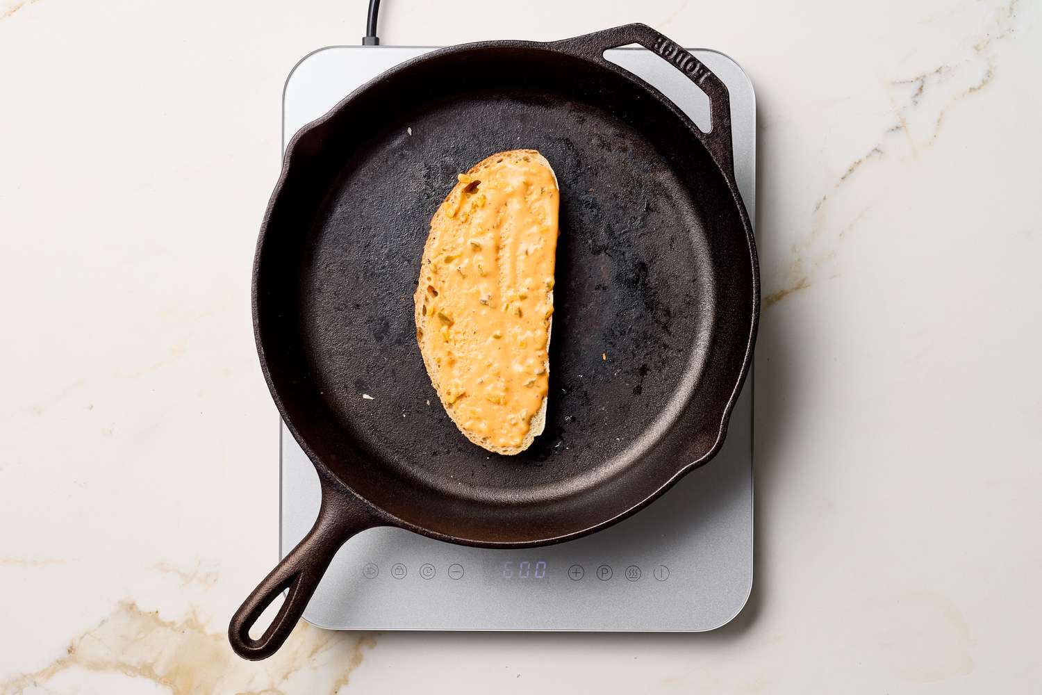 A grilled cheese sandwich being cooked in a cast iron skillet on a cooktop