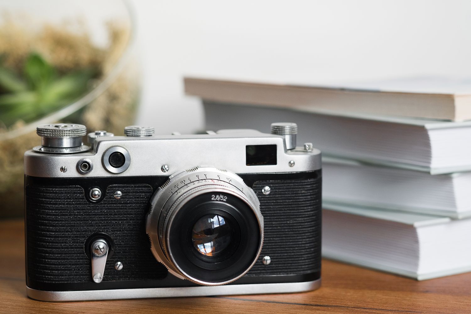 A vintage camera placed on a wooden surface with a stack of books and a glass decorative object in the background
