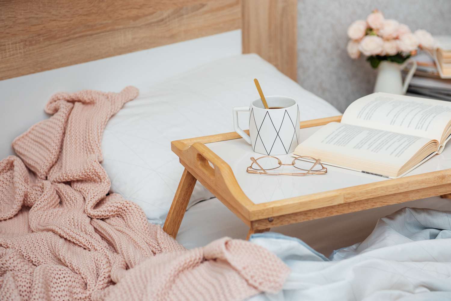 Cup of coffee, book and glasses on bed with soft blanket indoors. 