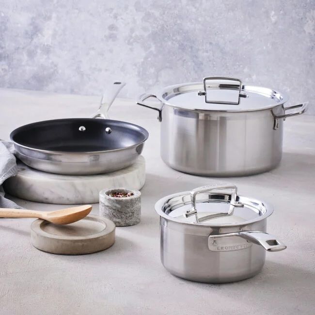 Set of stainless steel cookware including pots and a frying pan with a spoon on a countertop