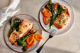 Two plates with salmon broccolini and slices of yam or carrot arranged as a meal photographed on a bright tabletop
