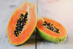 Two halves of a ripe papaya with seeds visible on a wooden surface