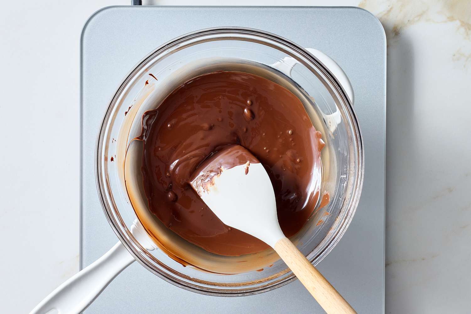 Bowl of melted chocolate with a spatula prepared on top of a metal surface