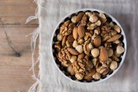 A bowl filled with mixed nuts placed on a wooden surface and a cloth napkin background