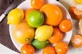 A bowl containing various citrus fruits including oranges lemons limes and tangerines arranged on a flat surface