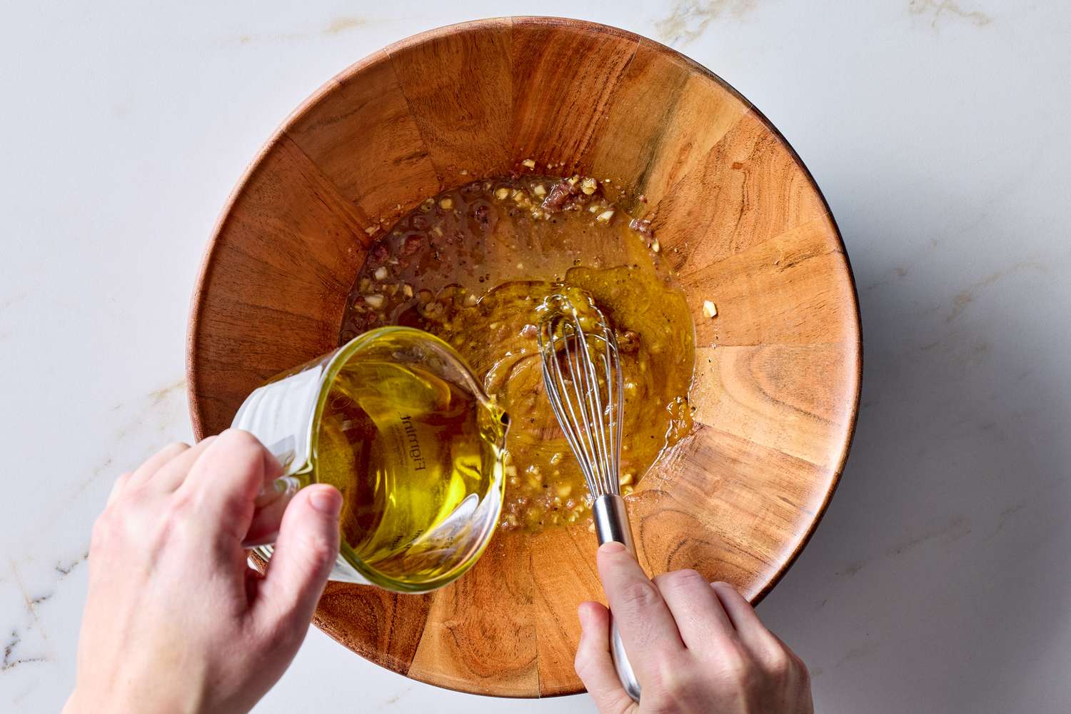 Mixing salad dressing in a wooden bowl pouring oil and whisking