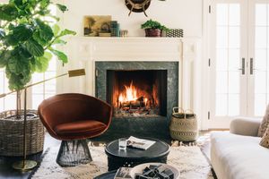 Cozy living room with a lit fireplace a round chair a coffee table and decor items such as plants and baskets arranged around the room