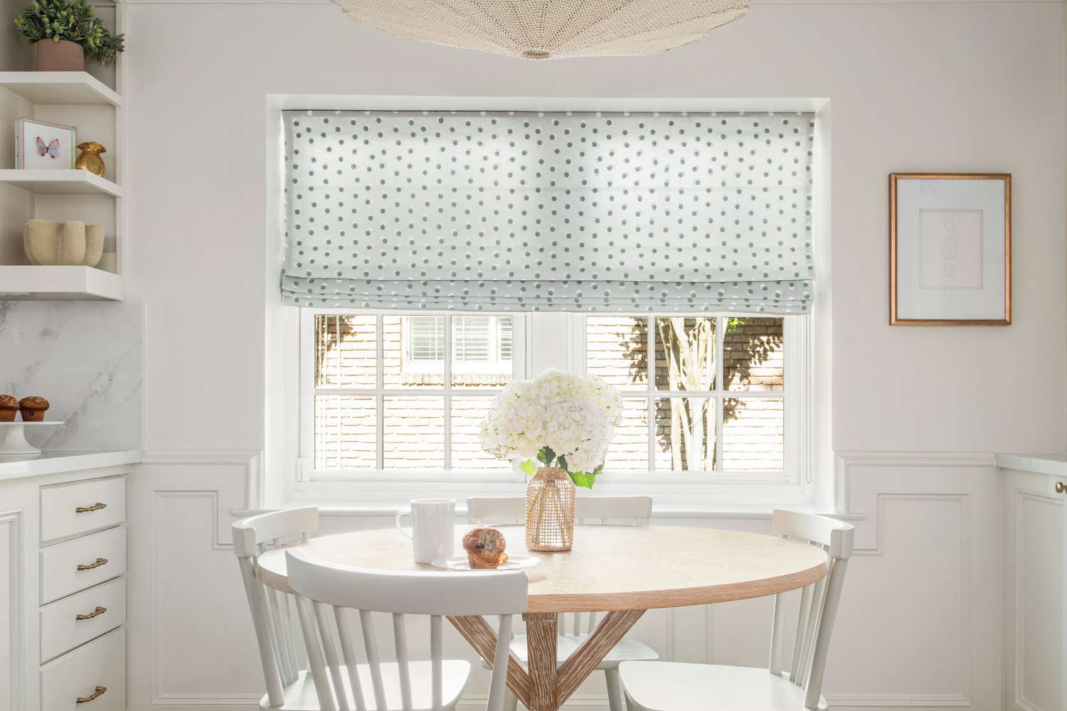 A dining table with white chairs a vase of flowers and a window with patterned blinds