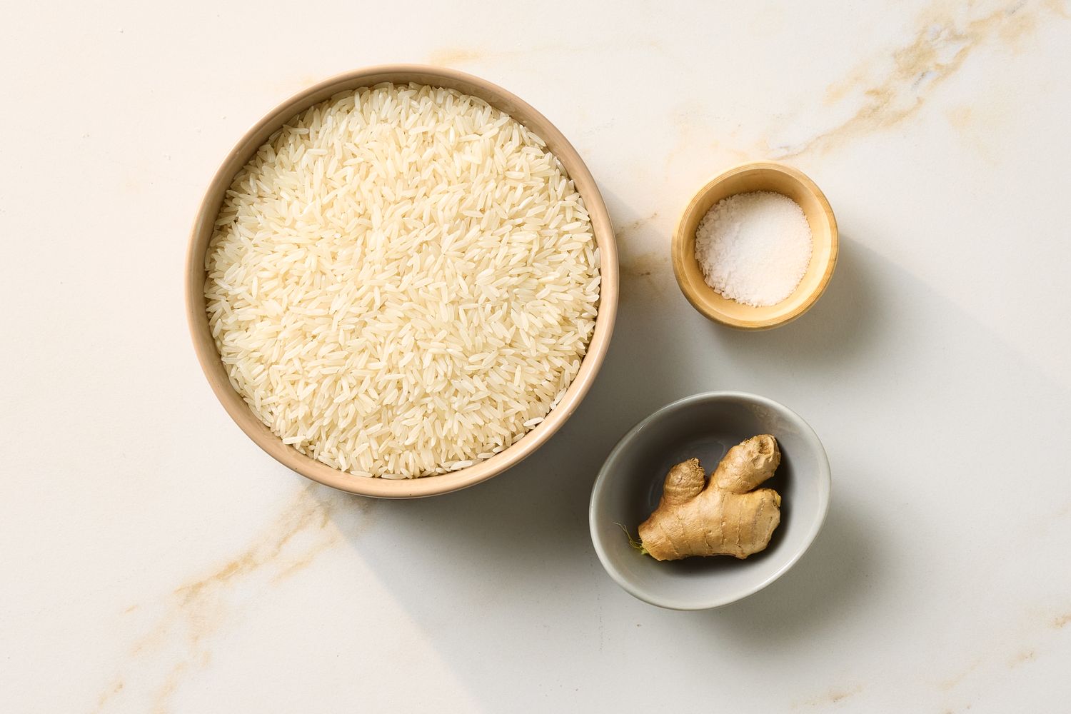 A bowl of rice a small bowl of salt and a ginger root piece displayed on a countertop