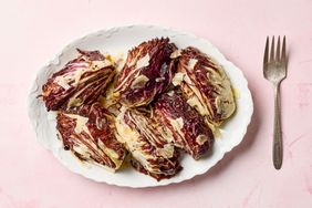 A plate of roasted radicchio wedges with shaved cheese on top displayed alongside a fork on a light background