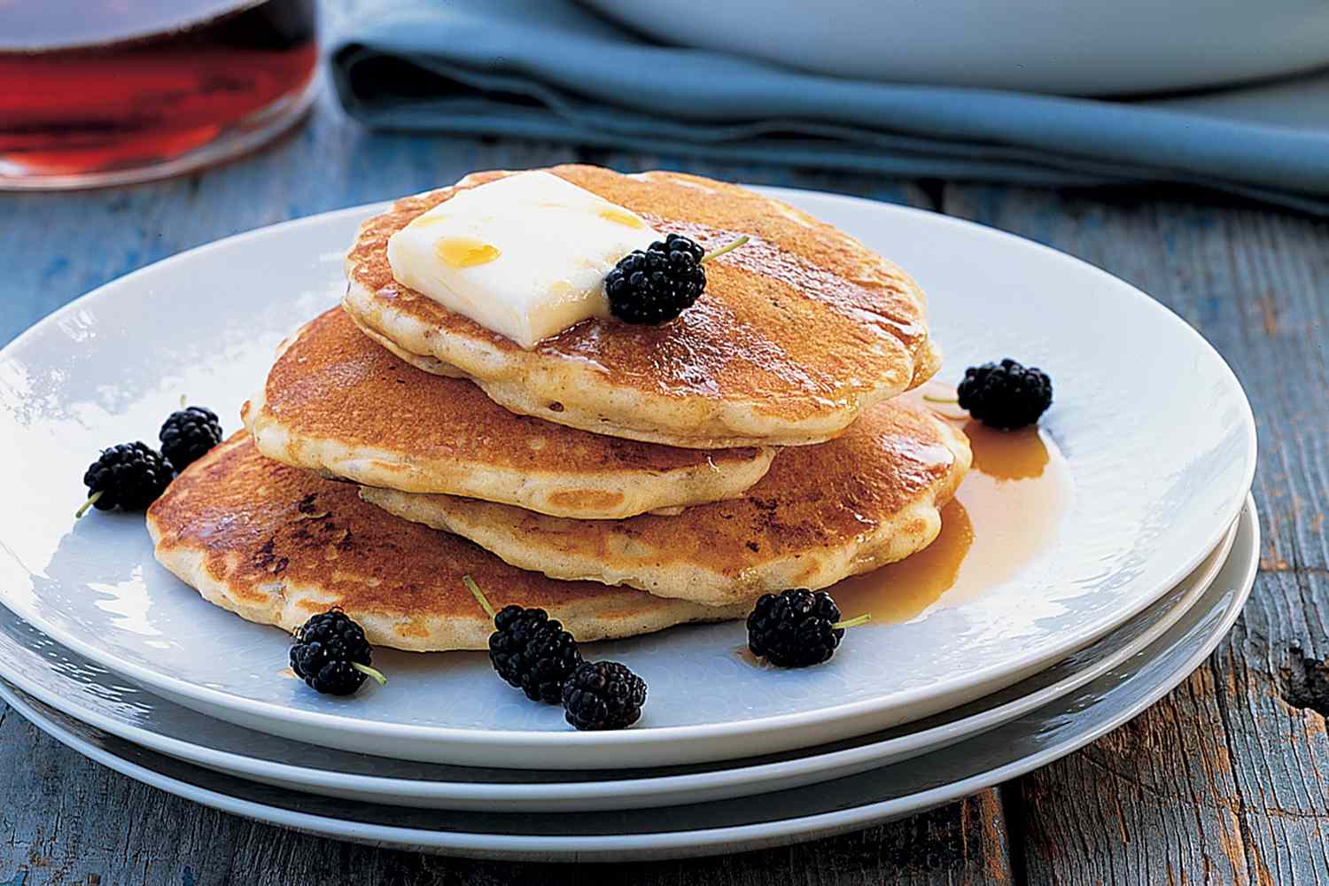Stack of pancakes with butter and blackberries on a plate served with syrup