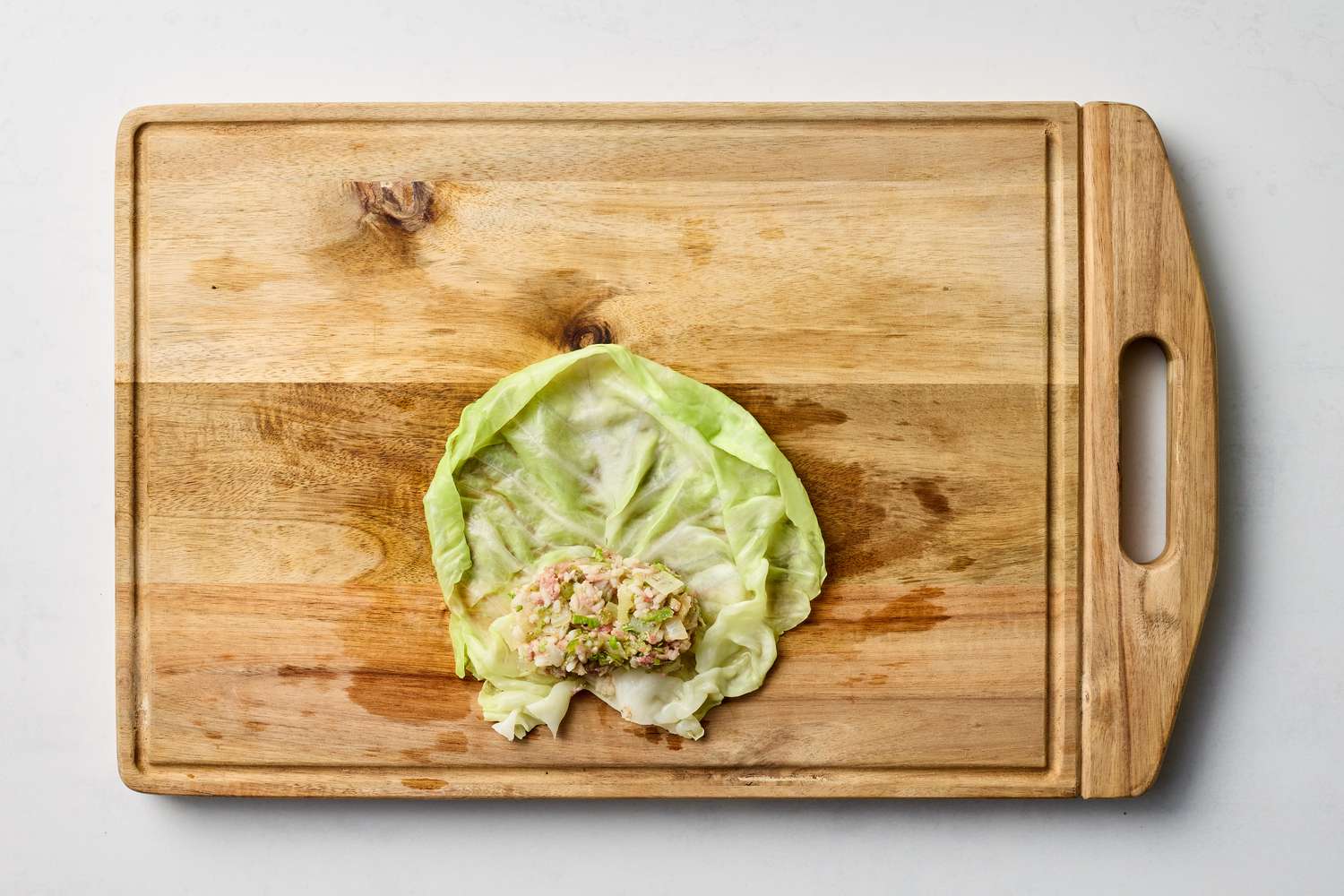 A cabbage leaf with a portion of stuffing placed on it lying on a wooden cutting board