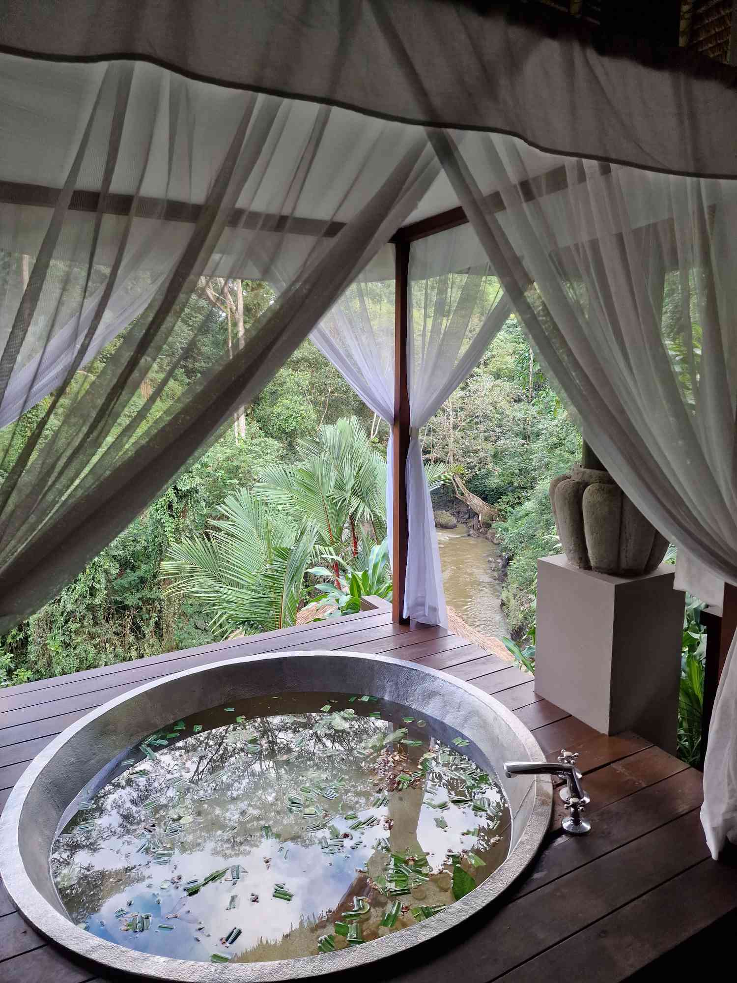 An outdoor soaking tub surrounded by curtains with a view of lush greenery