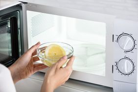 Hands placing a bowl containing a lemon slice into a microwave oven