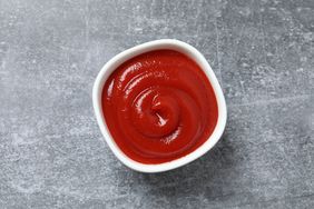A bowl of ketchup on a gray surface