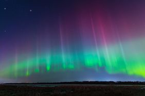 Aurora borealis with colorful light streaks in the night sky above a horizon with land and water