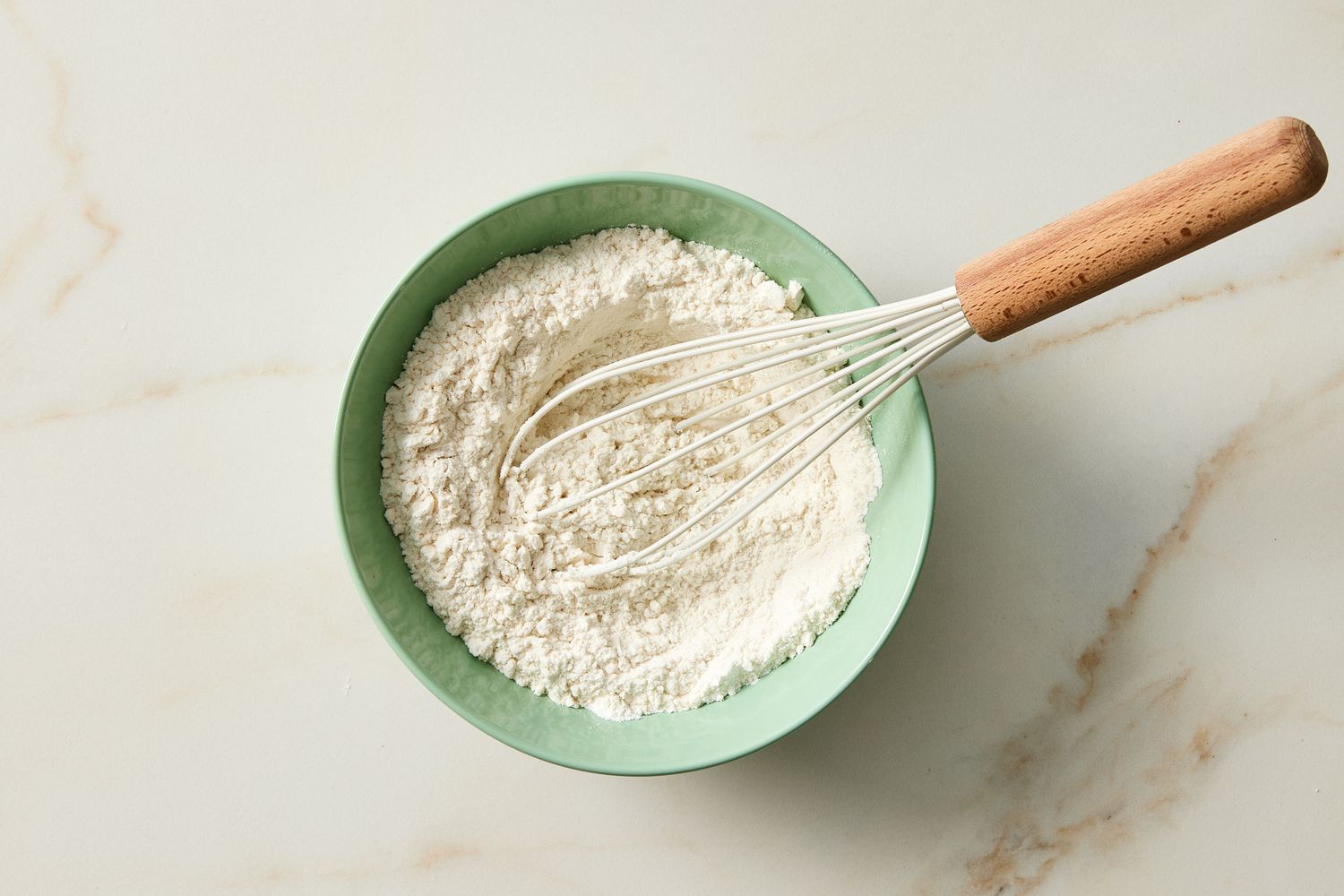 Dry ingredients for silver dollar pancakes in green bowl with whisk