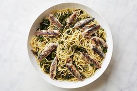 A plate of pasta topped with sardines and sauted greens highlighting a seafood pasta dish