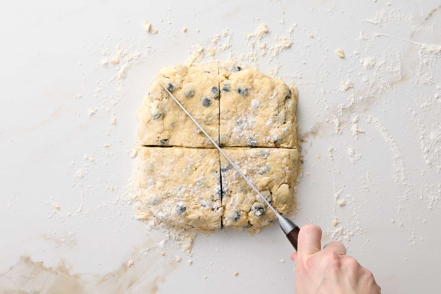 Hand cutting blueberry scone dough into four portions with a knife