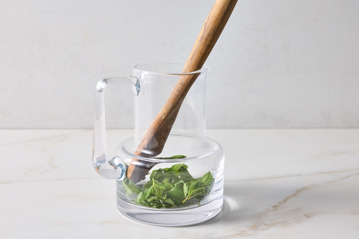 Glass pitcher with mint leaves and a wooden muddler