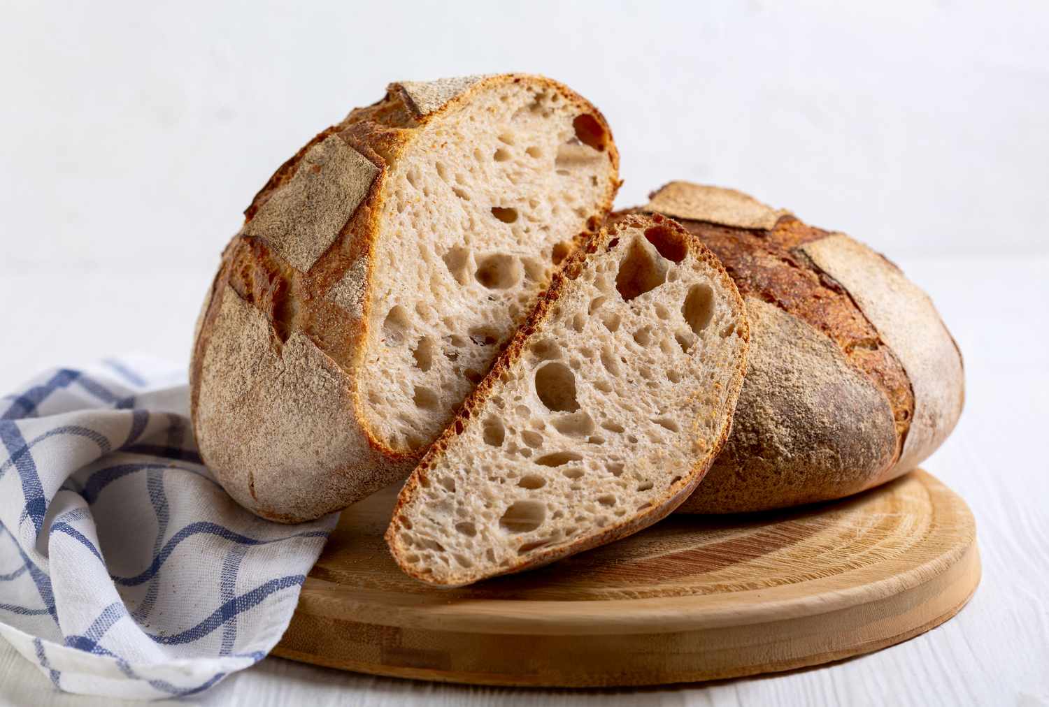 A sliced loaf of sourdough bread on a wooden board a cloth napkin beside it