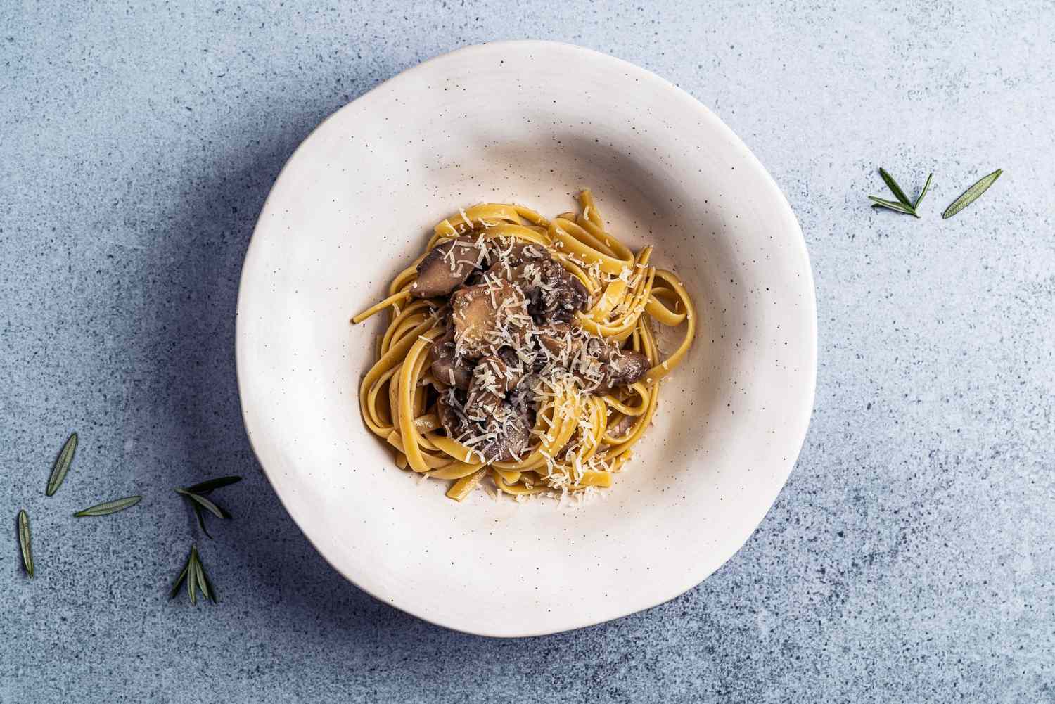 Bowl of mushroom and parmesan pasta on light blue background