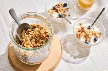 Granola in a glass jar with bowls of yogurt granola and blueberries