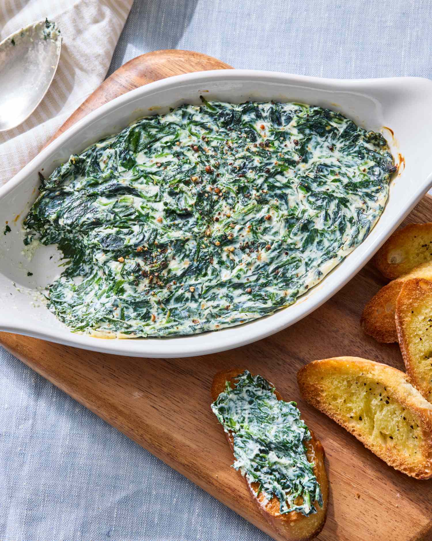 A serving dish with spinach dip and toasted bread slices on a cutting board