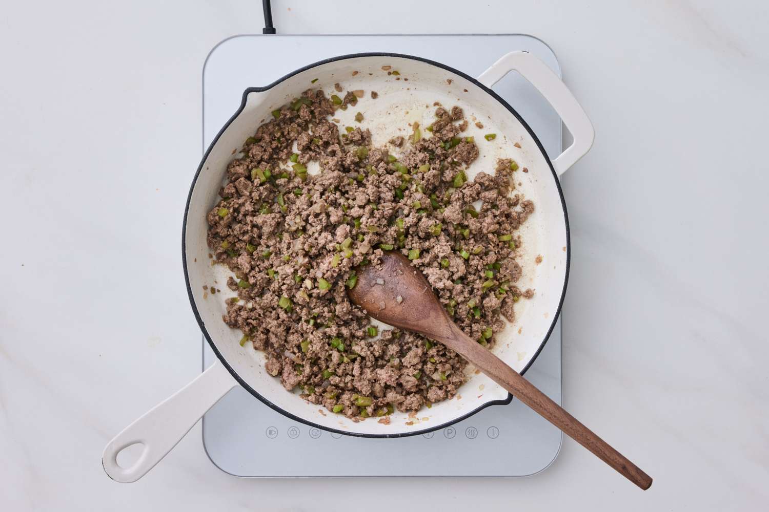 Cooking ground meat with green ingredients in a pan with a wooden spoon on an electric stovetop