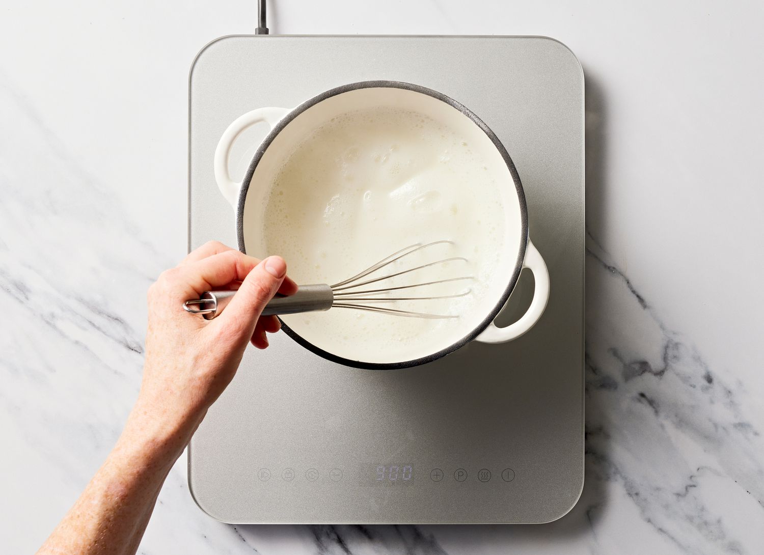 someone stirring white ingredients in a pot with a wisk