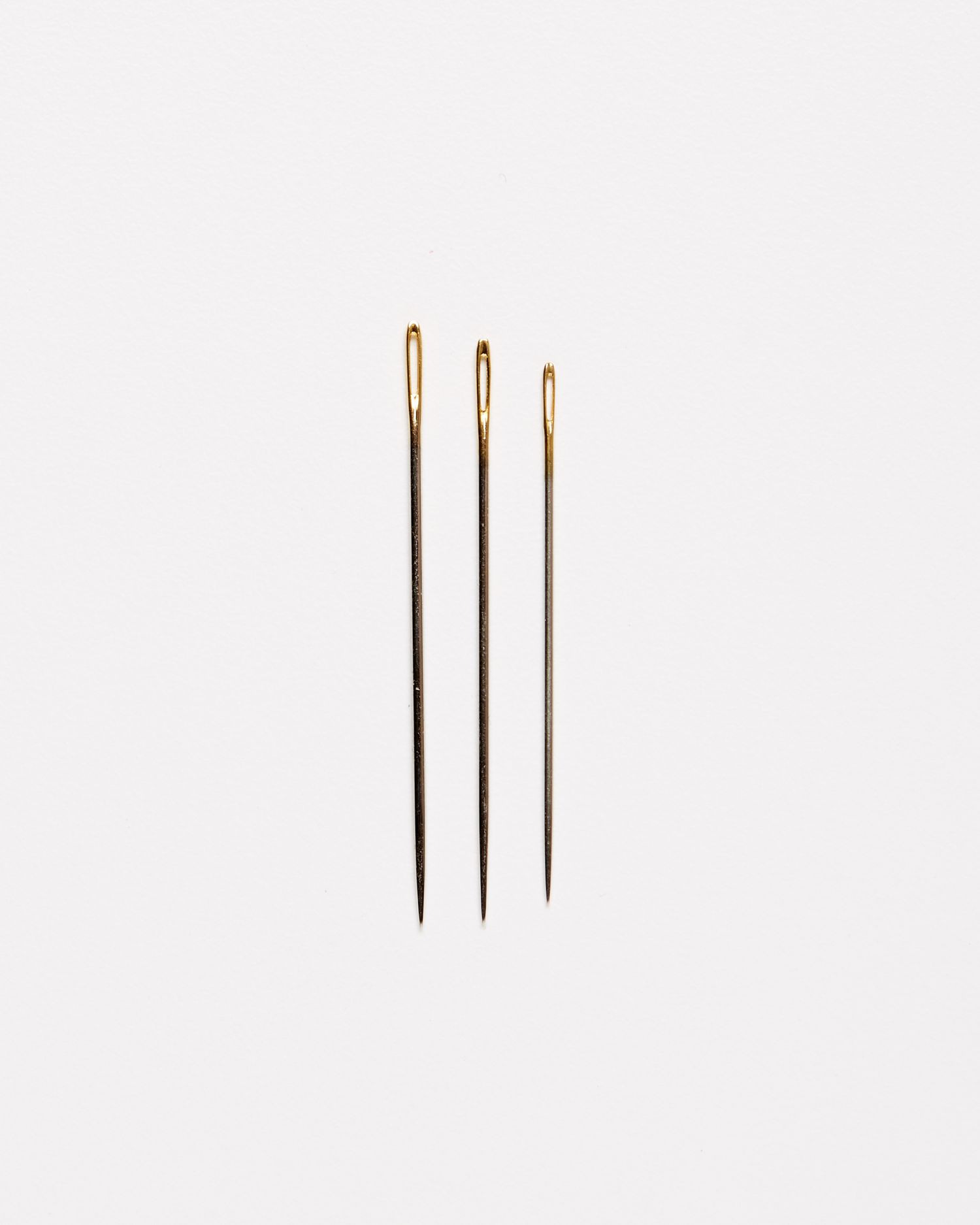 three embroidery quilting needles against a white background