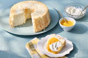 Angel food cake with a slice served, topped with whipped cream and a yellow sauce