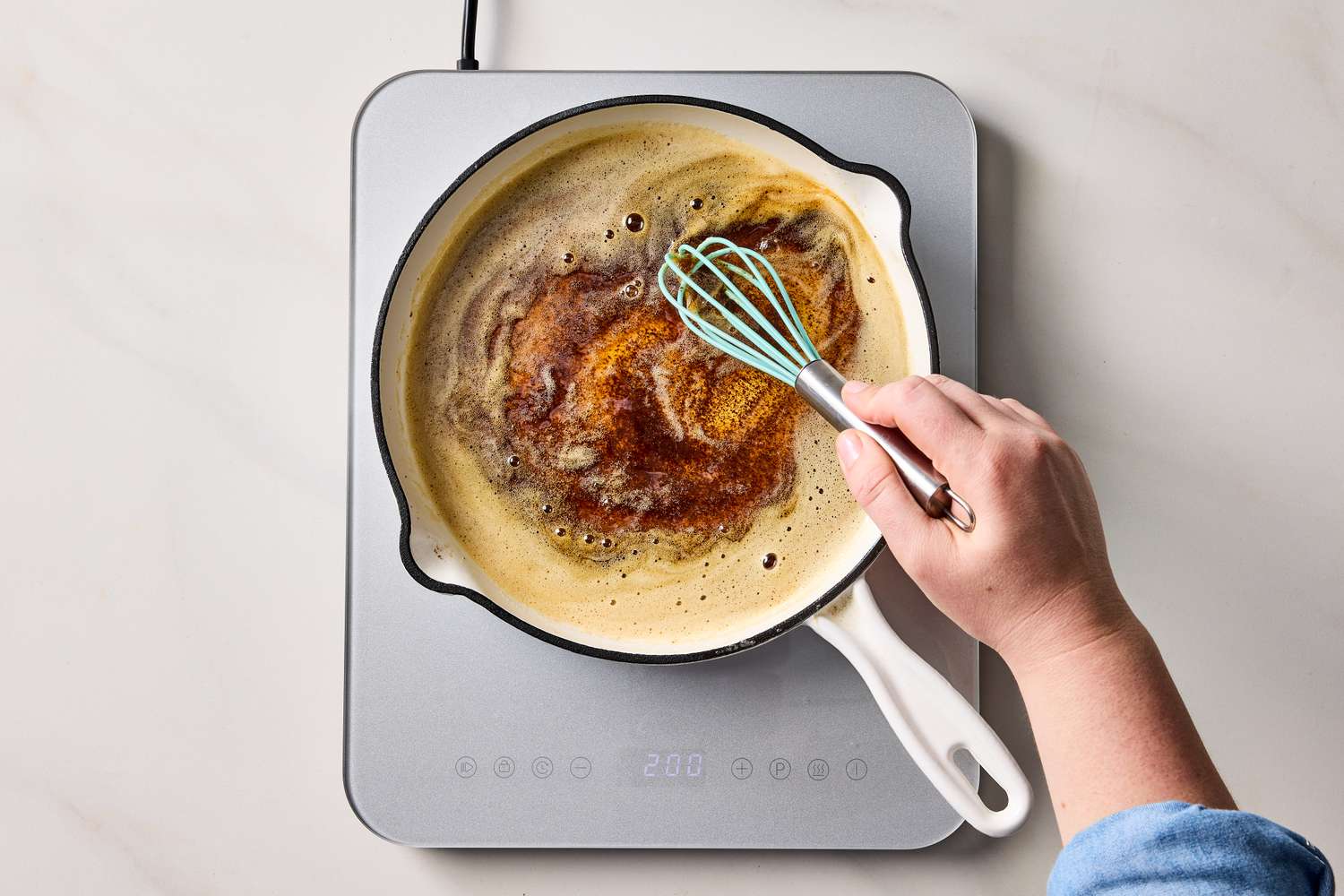 A hand whisking browned butter in a saucepan on an induction cooktop