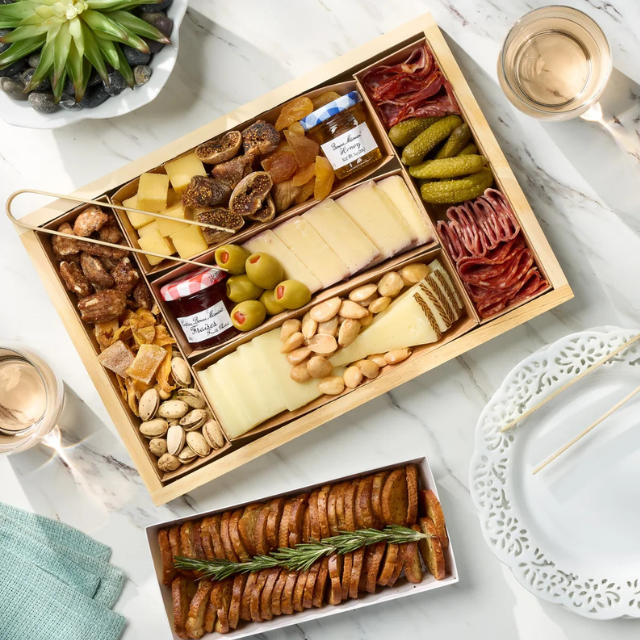 A charcuterie tray with arranged cheeses meats nuts and preserves alongside a platter of sliced bread