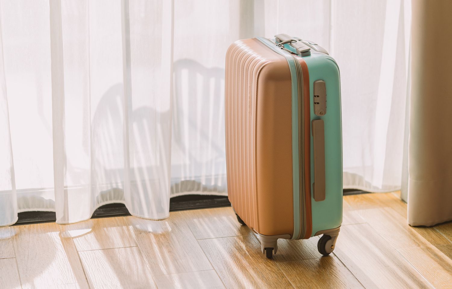 A suitcase standing upright indoors near a window with curtains