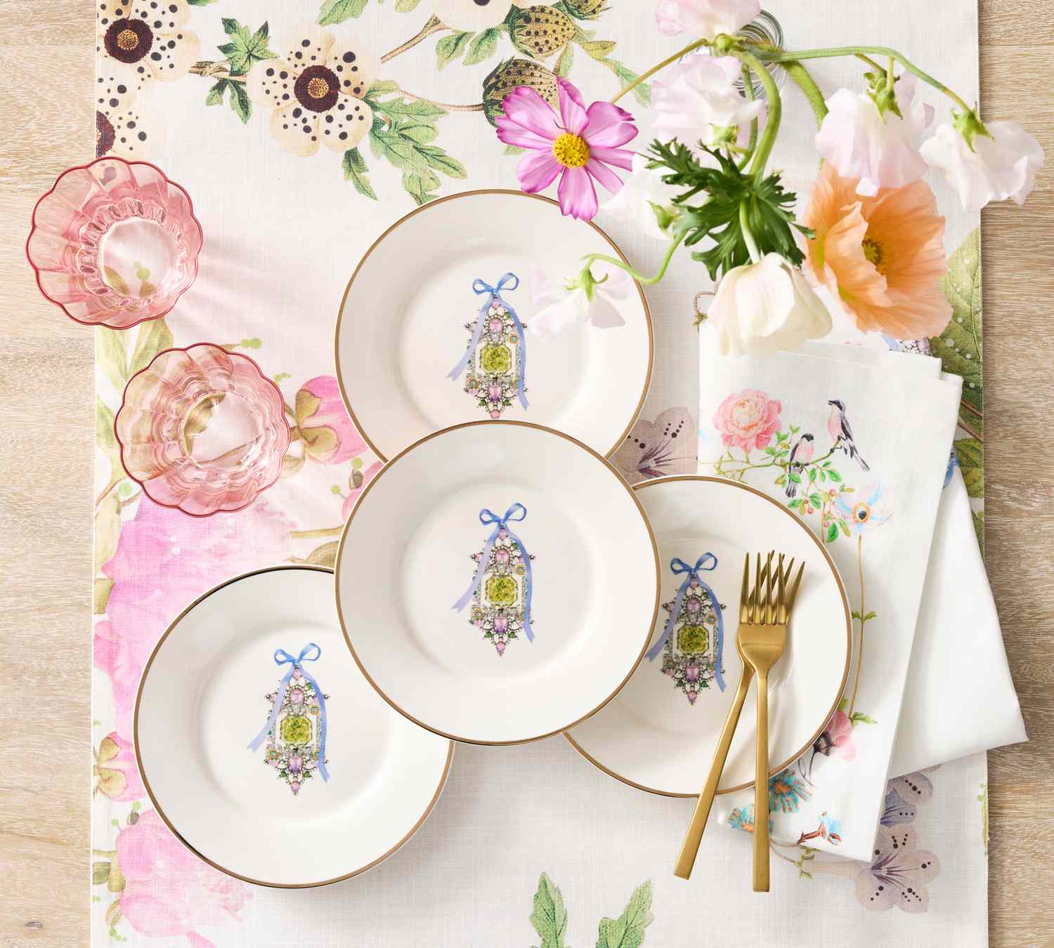 A collection of floral-themed dinnerware and linens with decorative plates and glasses arranged on a wooden surface