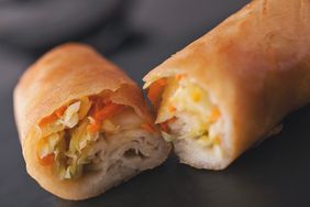 Two spring rolls one whole and one cut open to reveal filling served on a dark surface
