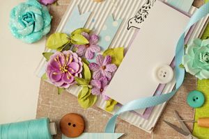 Scrapbooking elements including flowers ribbon buttons and paper arranged on a flat surface
