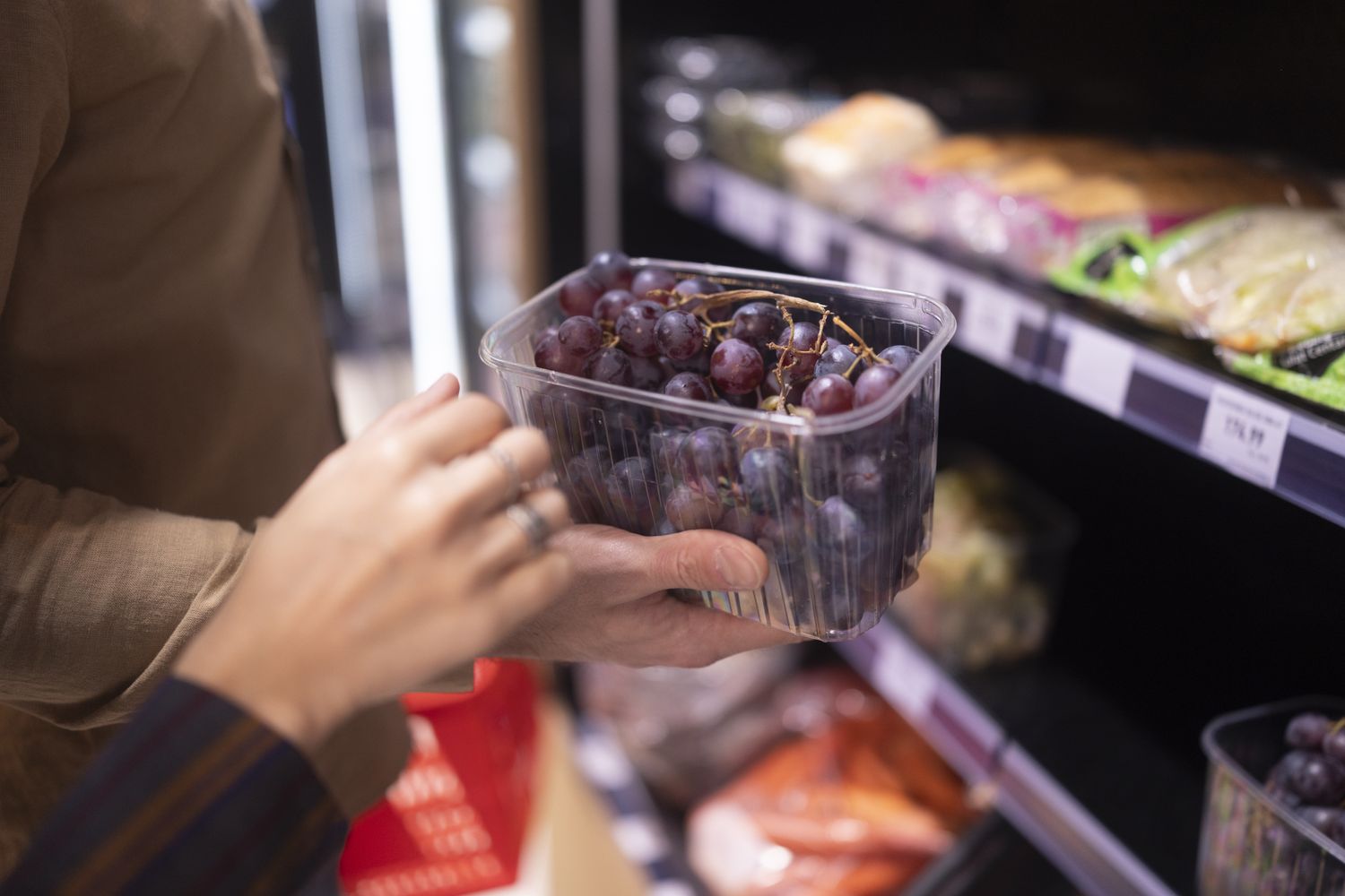 A person holding a container of grapes near a grocery store shelf