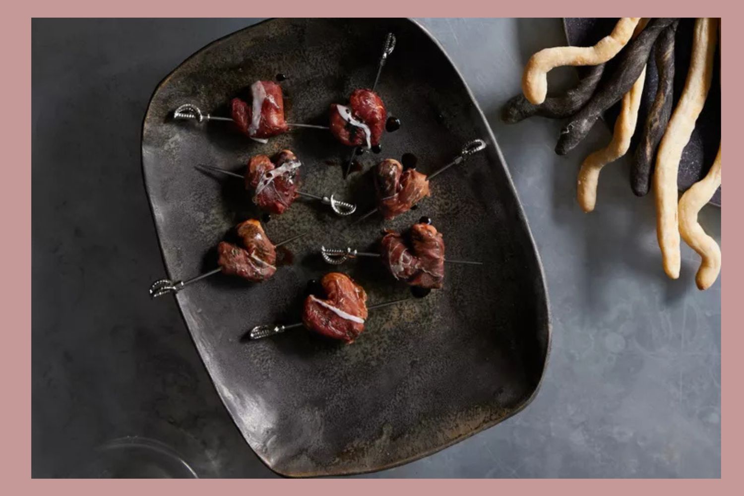 Plated dish featuring heartshaped appetizers on skewers paired with twisted breadsticks on the side