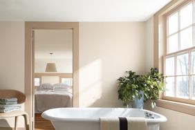 Bathroom with freestanding tub towel potted plant and view of a bedroom through an open doorway