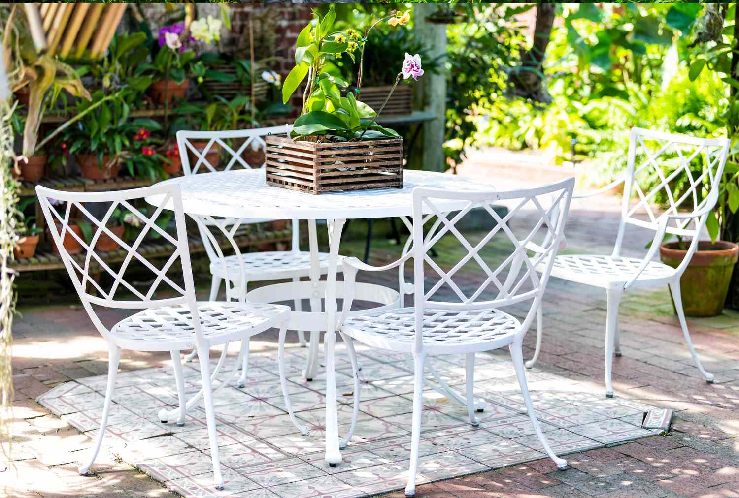 Outdoor patio set with a white metal table and chairs surrounded by greenery and featuring a potted plant on the table