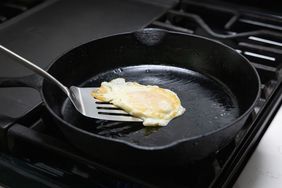 A fried egg in a cast iron skillet with a spatula lifting it on a stovetop