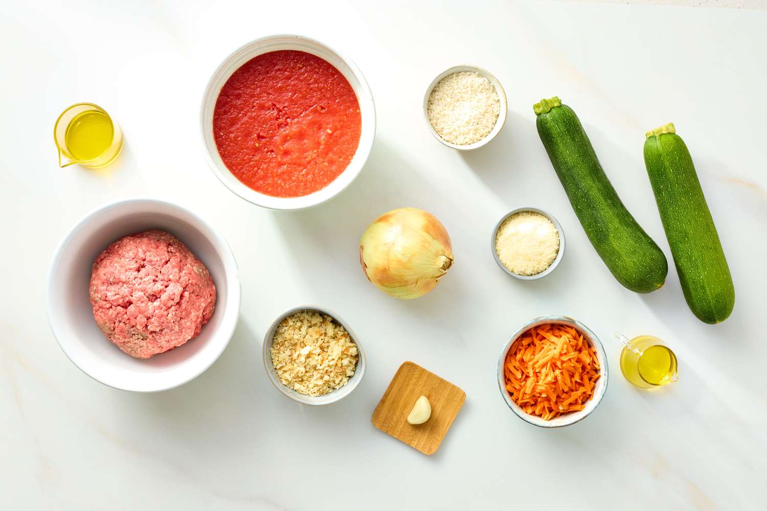 Ingredients arranged on a countertop including zucchini ground meat tomato sauce onion and garlic