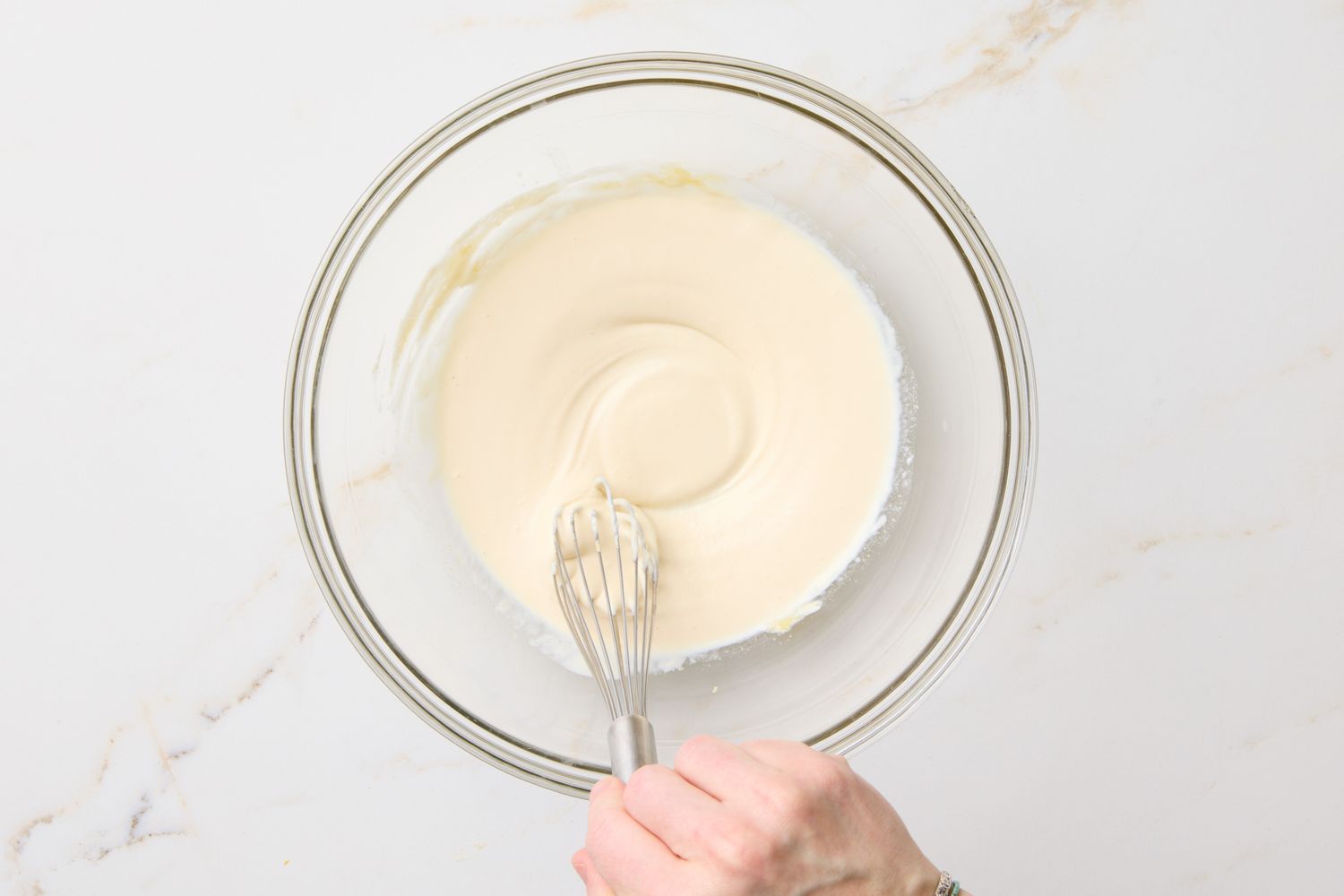A mixing bowl of creamy coleslaw dressing being whisked by a hand